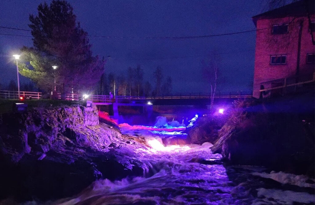 Voimalaitoksen virtaava vesi valaistuna violeteilla valoilla.